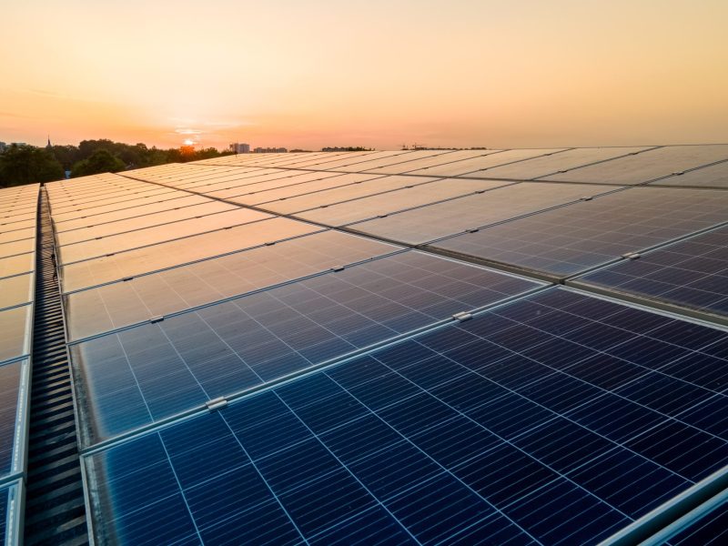 Blue photovoltaic solar panels mounted on building roof for producing clean ecological electricity at sunset. Production of renewable energy concept.