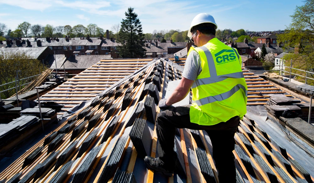 Roofing contractor installing slate tiles on a heritage pitched roof during a refurbishment project.
